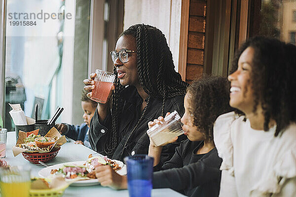 Lächelnde Frau genießt Essen und Getränke mit Kindern  während sie im Restaurant sitzt