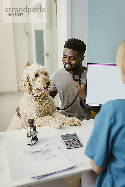 Lächelnder Mann mit Labradoddle blickt die Tierärztin in der Tierklinik an