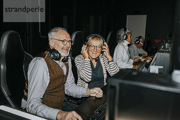 Smiling senior couple playing video game by male and female friends in gaming lounge