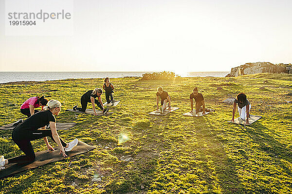 Team macht Dehnübungen auf Gras während einer Gruppentrainingseinheit am Meer gegen den Himmel