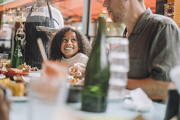 Lächelndes Mädchen beim Essen mit Vater  während es im Restaurant sitzt