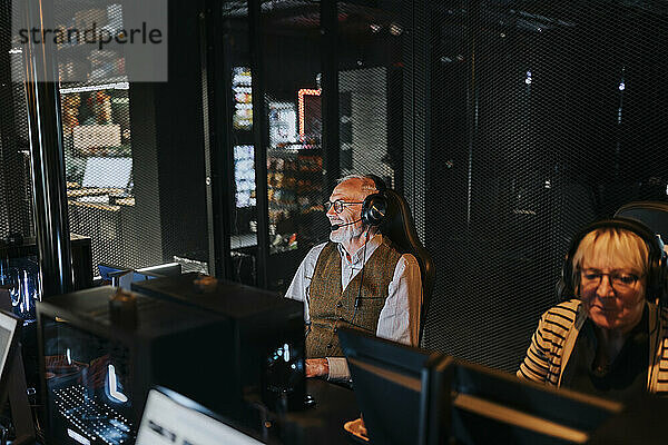 Älterer Mann mit Headset sitzt neben einer Freundin und spielt in der Gaming-Lounge ein Videospiel am Computer