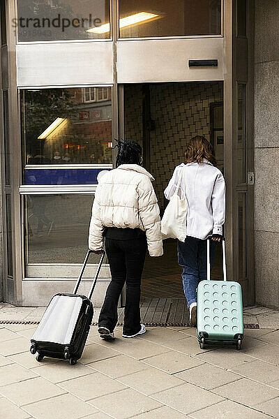Rückansicht junger weiblicher Touristen mit Rollgepäck  die das Hotel betreten