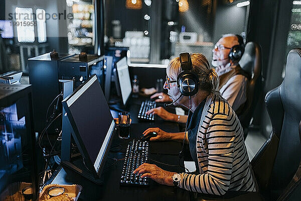 Ältere Frau spielt von einem männlichen Freund in der Gaming-Lounge ein Videospiel am Computer