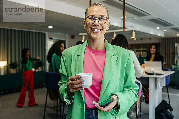 Porträt einer glücklichen Geschäftsfrau  die im Büro eine Kaffeetasse hält
