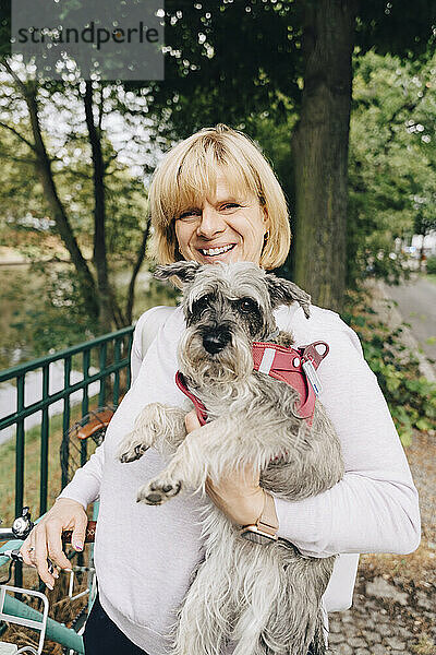 Porträt einer lächelnden blonden Frau mit süßem Hund im öffentlichen Park