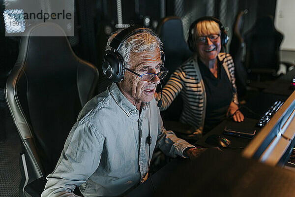 Älterer Mann mit Headset spielt Videospiel einer Freundin im Gaming-Center