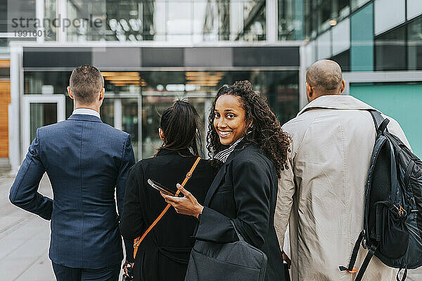 Seitenansichtporträt einer lächelnden Geschäftsfrau  die mit Kollegen vor dem Gebäude über die Schulter schaut