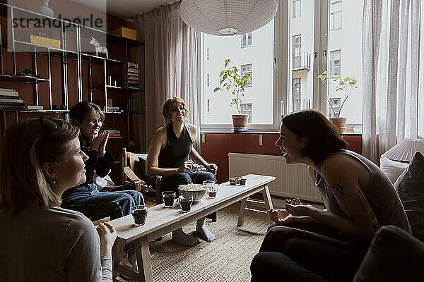 Fröhliche Freundinnen genießen Snacks und Getränke  während sie in der Wohnung sitzen