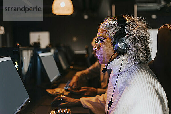 Seitenansicht einer älteren Frau  die im Gaming-Center ein Videospiel am Computer spielt