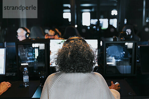 Rückansicht einer älteren Frau  die im Gaming-Center ein Videospiel spielt