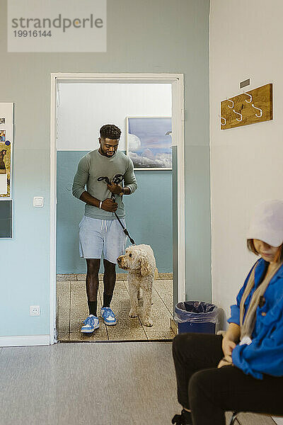 Young man walking labradoddle while waiting in veterinary clinic
