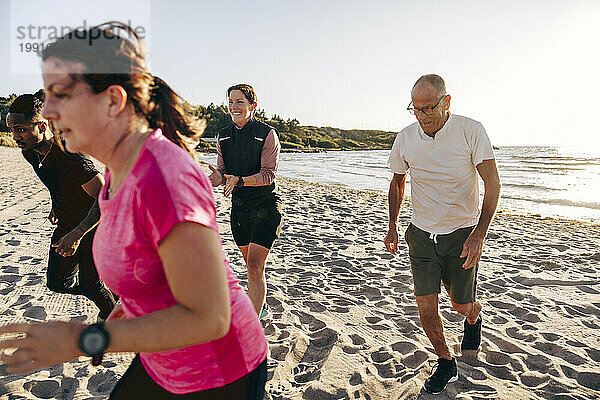 Lächelnde weibliche Trainerin jubelt dem Team während der Gruppentrainingseinheit am Strand zu
