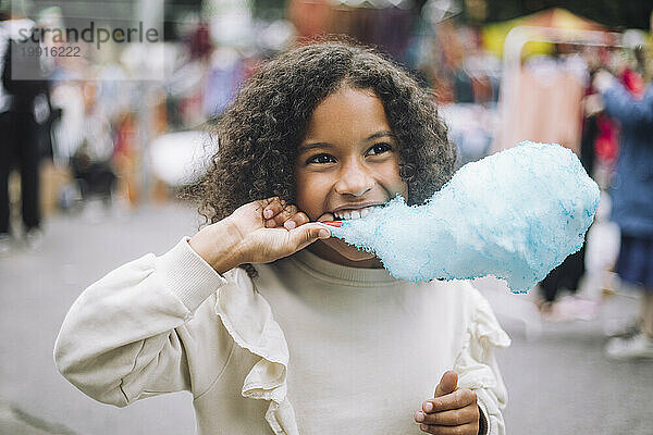 Nachdenkliches Mädchen isst blaue Zuckerwatte im Vergnügungspark