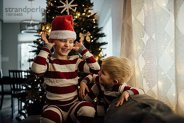 Kleine Jungen  die Weihnachtspyjamas und eine Weihnachtsmütze tragen  machen das albern