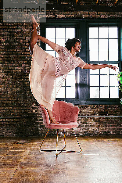 Schwarze Tänzerin in gespaltener Pose auf einem Stuhl im Kleid