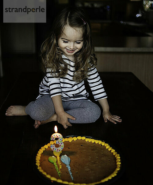 Glückliches kleines Mädchen  das Geburtstagstorte in der Küche betrachtet