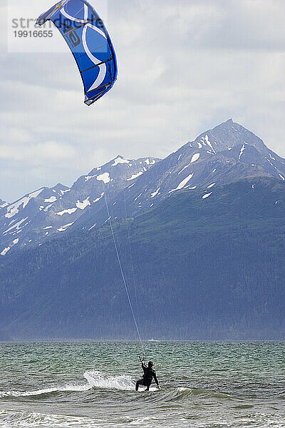 Ein mittlerer Erwachsener reitet beim Kitesurfen in Homer  Alaska  vom Strand aus.