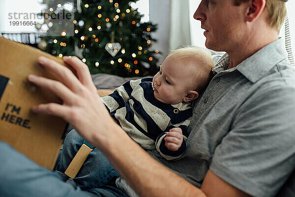 Baby Junge sitzt auf Papas Schoß und öffnet Weihnachtsgeschenke in f