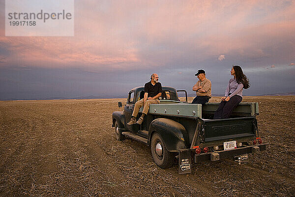 Ein Lastwagen aus dem Jahr 1959 bietet Platz für drei Personen und genießt den Sonnenuntergang von einem Feld auf einer Farm in Amsterdam  Montana.