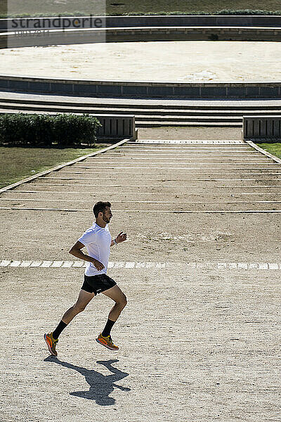 Seitenansicht eines fitten Mannes  der neben einem antiken Sportstadion läuft.