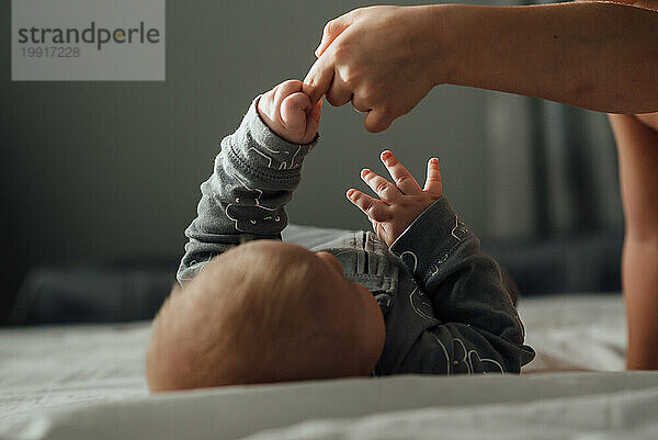 Blick von oben auf das Baby  das nach dem Finger seines Geschwisterkindes greift  witzig