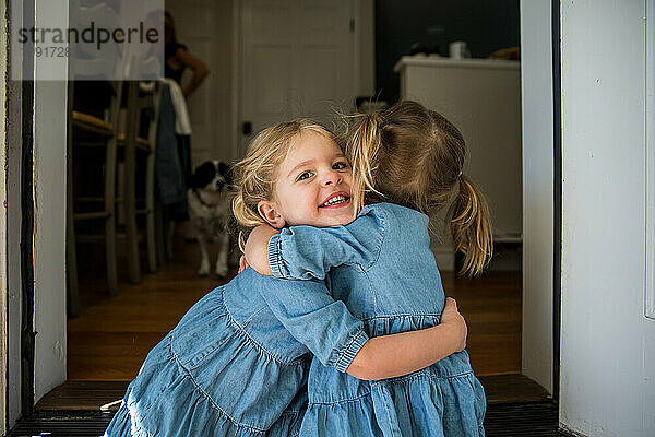 Junge Schwestern passen zusammen und umarmen sich im Türrahmen