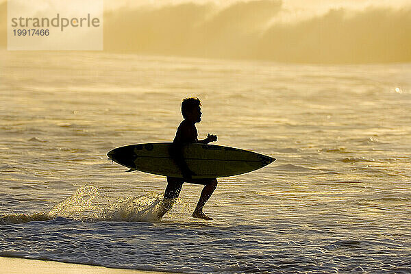 Silhouette eines Mannes mit Surfbrett  der in Hawaii in die Brandung rennt