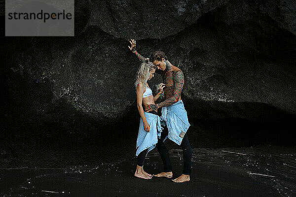 Junges schönes Paar am schwarzen Sandstrand  Bali. Tätowierter Mann.
