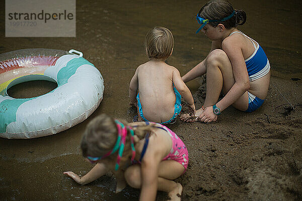 Drei kleine Kinder spielen am Flussufer mit einem Schlauch