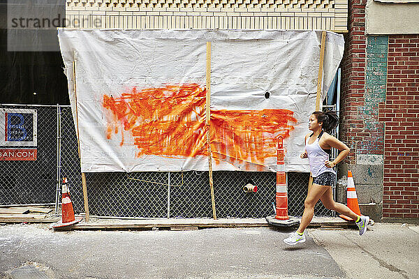 Eine junge asiatische Frau rennt an einer Baustelle auf einer Stadtstraße vorbei.