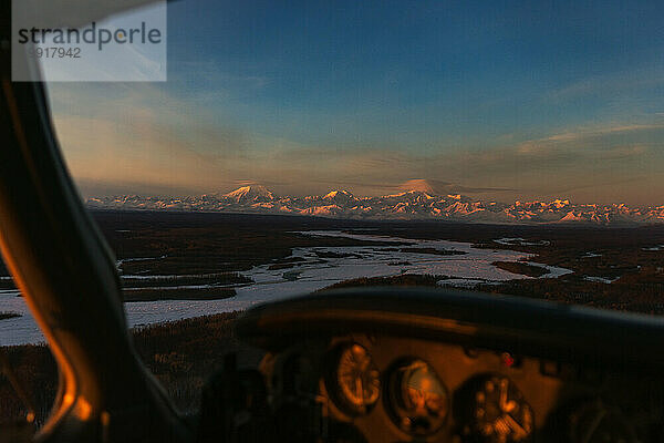 Die Sonne geht über dem Alaska-Gebirge unter  gesehen durch ein Flugzeugfenster