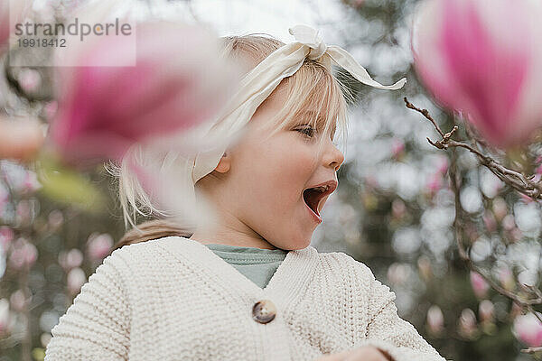 Nettes kleines blondes Mädchen in Magnolienblüten