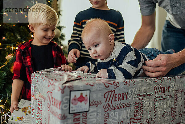 Der kleine Junge liegt auf dem Weihnachtsgeschenk  während die Familie ihm hilft