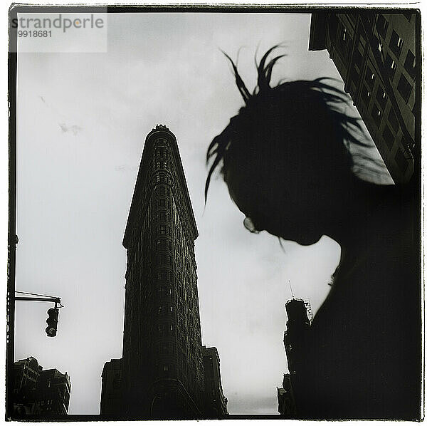 Eine Silhouette mit Dreadlocks und Brille steht vor dem Flat Iron Building in New York City.