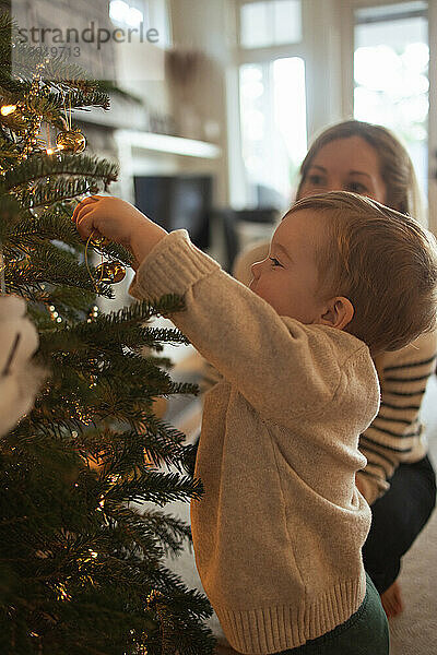 Mutter und Kleinkind schmücken fröhlich den Weihnachtsbaum der Familie