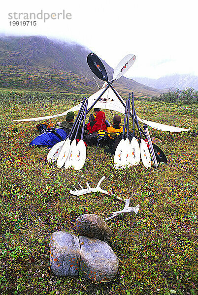 Expeditionsteilnehmer entspannen sich an einem regnerischen Tag an einem Fluss im Arctic National Wildlife Refuge  Alaska  unter der Plane.
