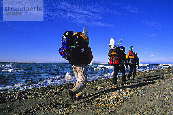 Drei Wanderer tragen ihre Packflöße am Strand von Barter Island am Rande der Beaufortsee in Alaska.