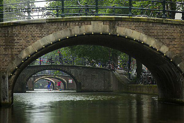 Zwei Personen paddeln im Stadtkanal unter Bogenbrücken  Amsterdam  Amsterdam  Niederlande