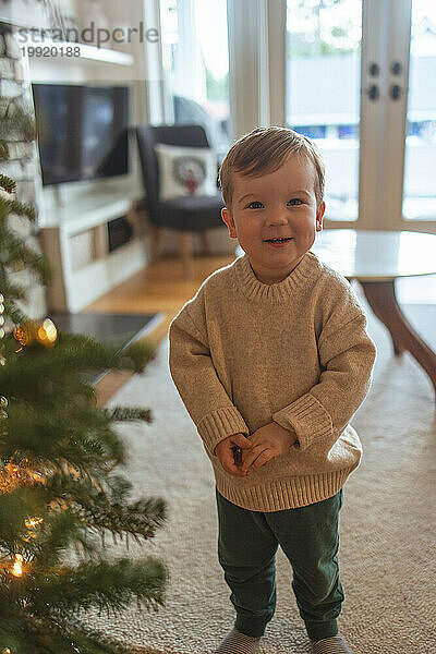 Kleiner Junge strahlt vor festlicher Freude neben dem Weihnachtsbaum