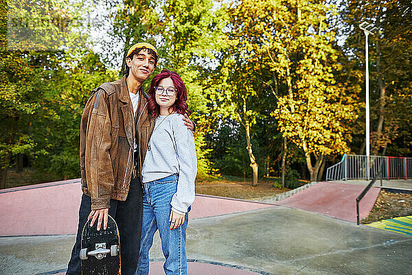 Lächelndes Mädchen und Junge mit einem Skateboard  die in einem Skatepark stehen