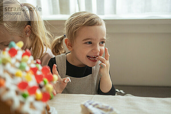 Junges Mädchen kichert  während es den Zuckerguss des Lebkuchenhauses probiert