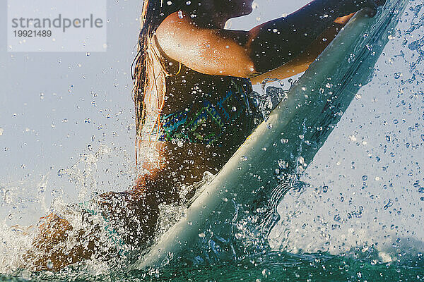 Eine Surferin im Bikini geht auf ihrem Surfbrett über eine brechende Welle