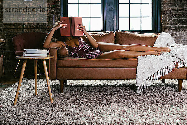 Gemischte Rassen-Tänzerin im rosa Trikot auf der Couch und liest ein Buch
