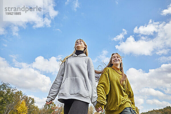 Zwei fröhliche junge Mädchen laufen Hand in Hand gegen den Himmel