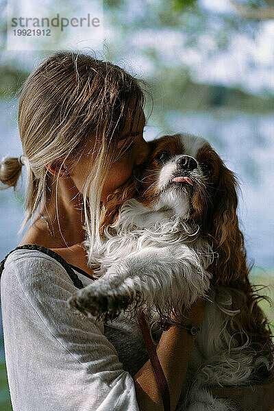 Junge Frau geht mit Hund am See spazieren  küsst den Hund.
