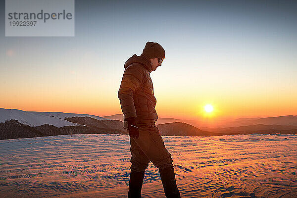 Junger Mann wandert bei Sonnenuntergang in den Winterbergen