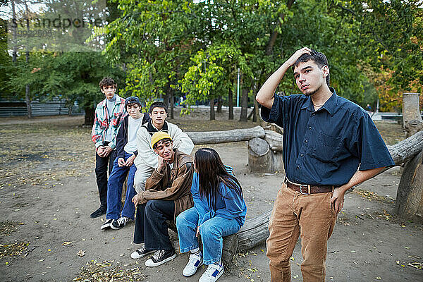 Nachdenklicher junger Mann  der in einer Gruppe von Freunden im Park steht