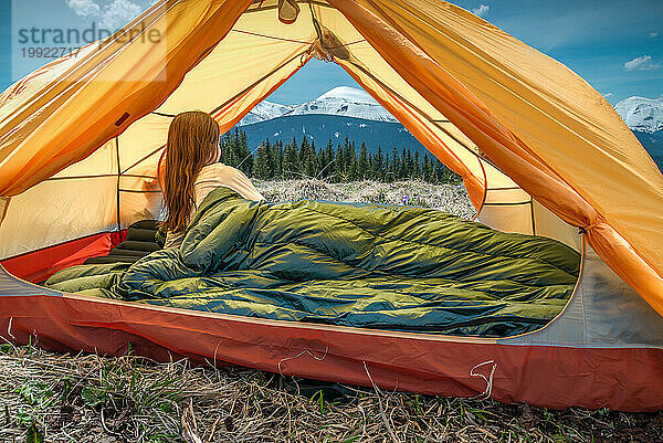 Eine Camperin im Zelt mit Blick auf die Berge in der Ferne