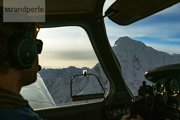 Ein männlicher Pilot blickt beim Flug in Alaska aus dem Fenster auf die Berge